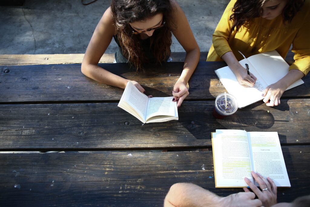 Three people seated around a wooden table, reading books, viewed from above.