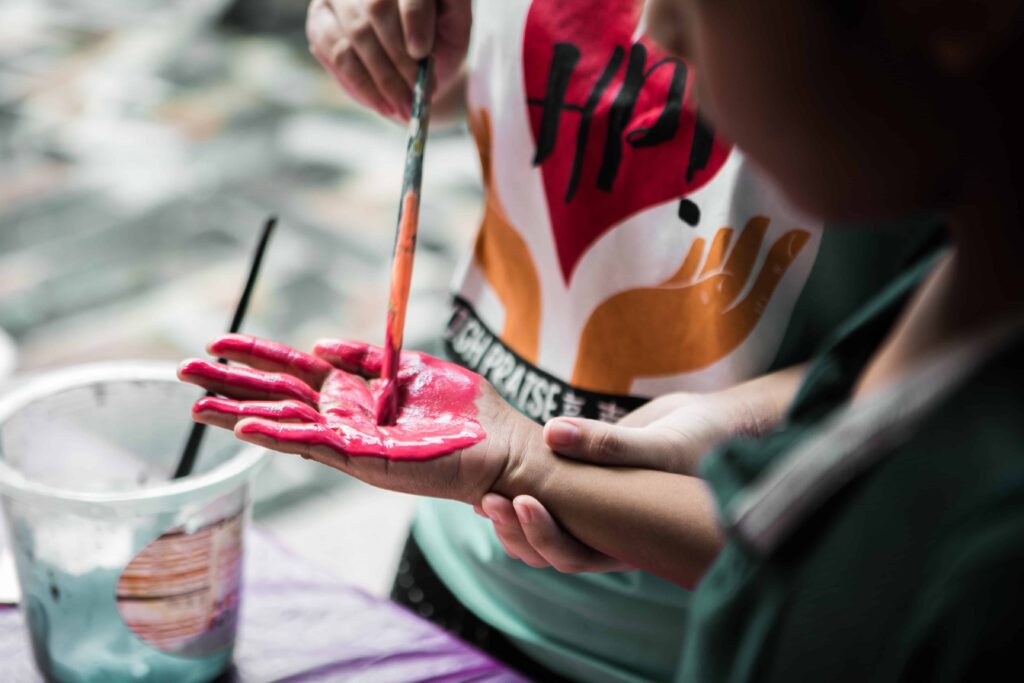 A kid painting another kids hand with pink paint.