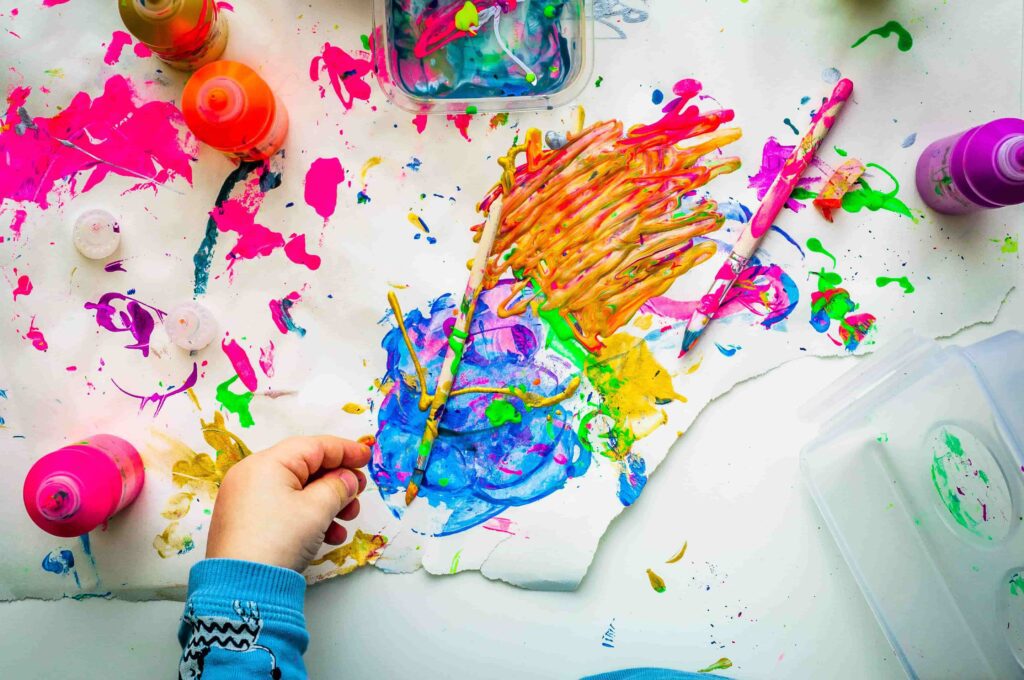 A child's hand painting with a brush on a white surface, showcasing creativity and artistic expression.