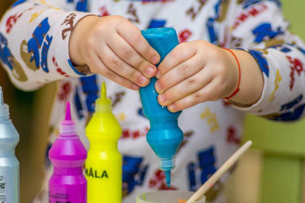 Kid squeezing a blue paint tube.