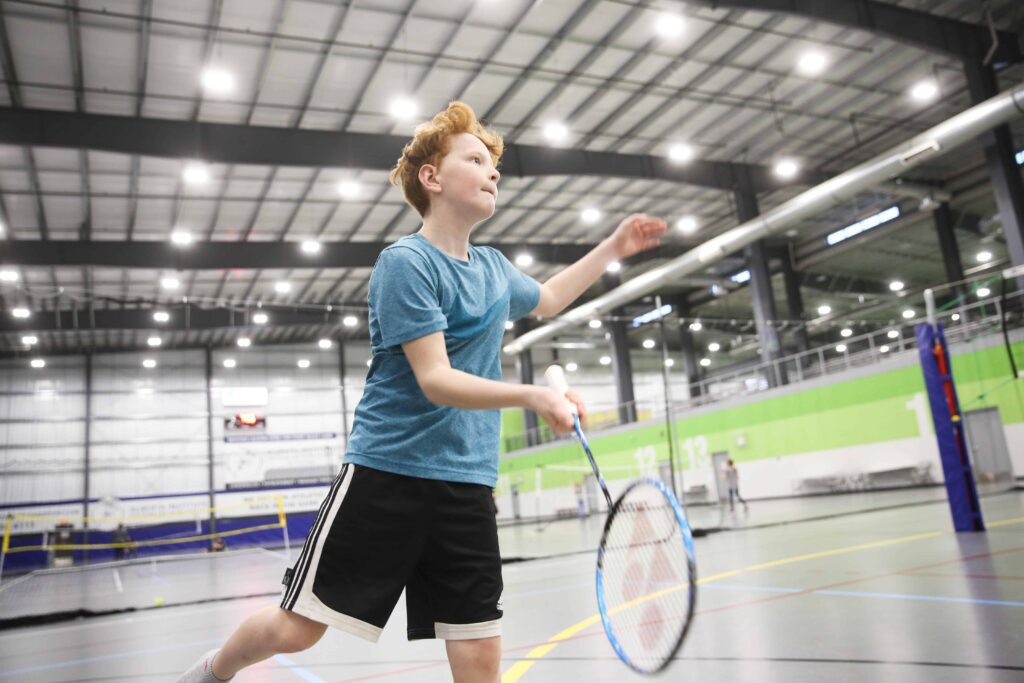 A boy playing badminton in an indoor gym, showcasing his skills and passion for the sport.