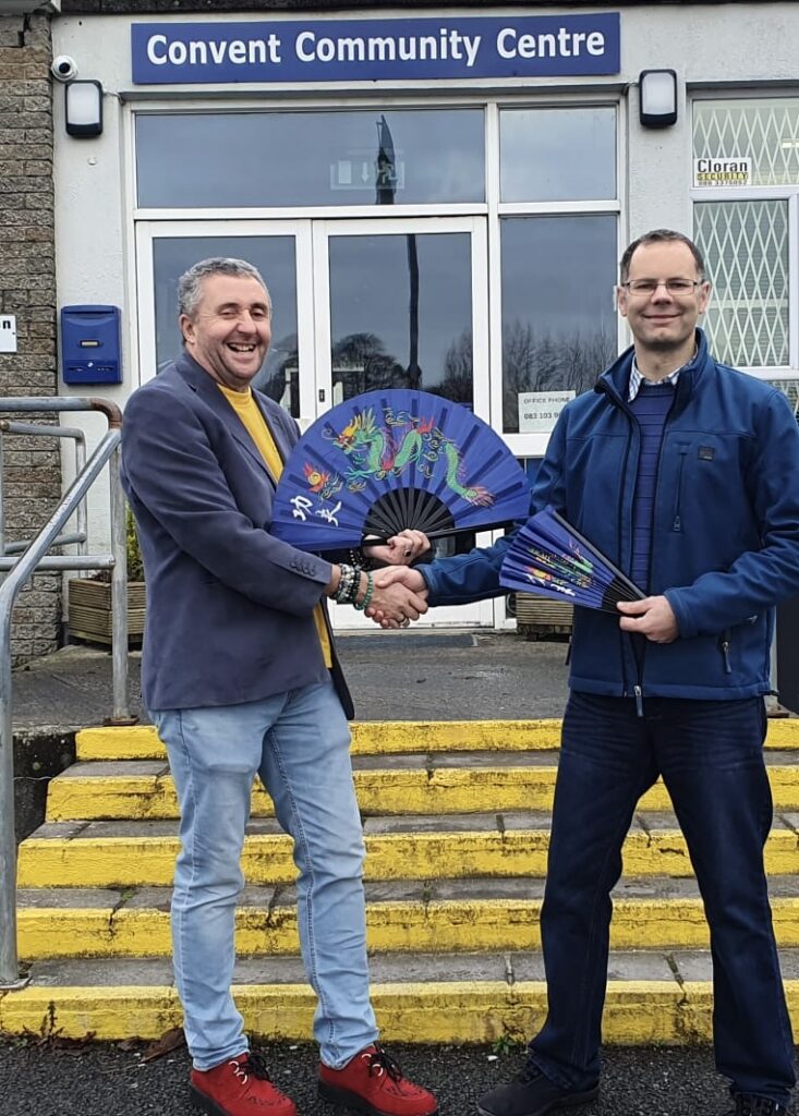 Two men shaking hands in front of Athboy CCC building, with one being a tai chi instructor.