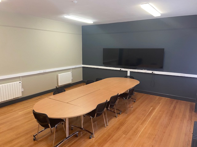 A conference table with chairs and a screen in a well-lit room, ready for a productive meeting.