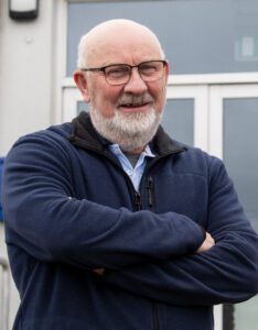 A man standing outside a community center, looking towards the camera.