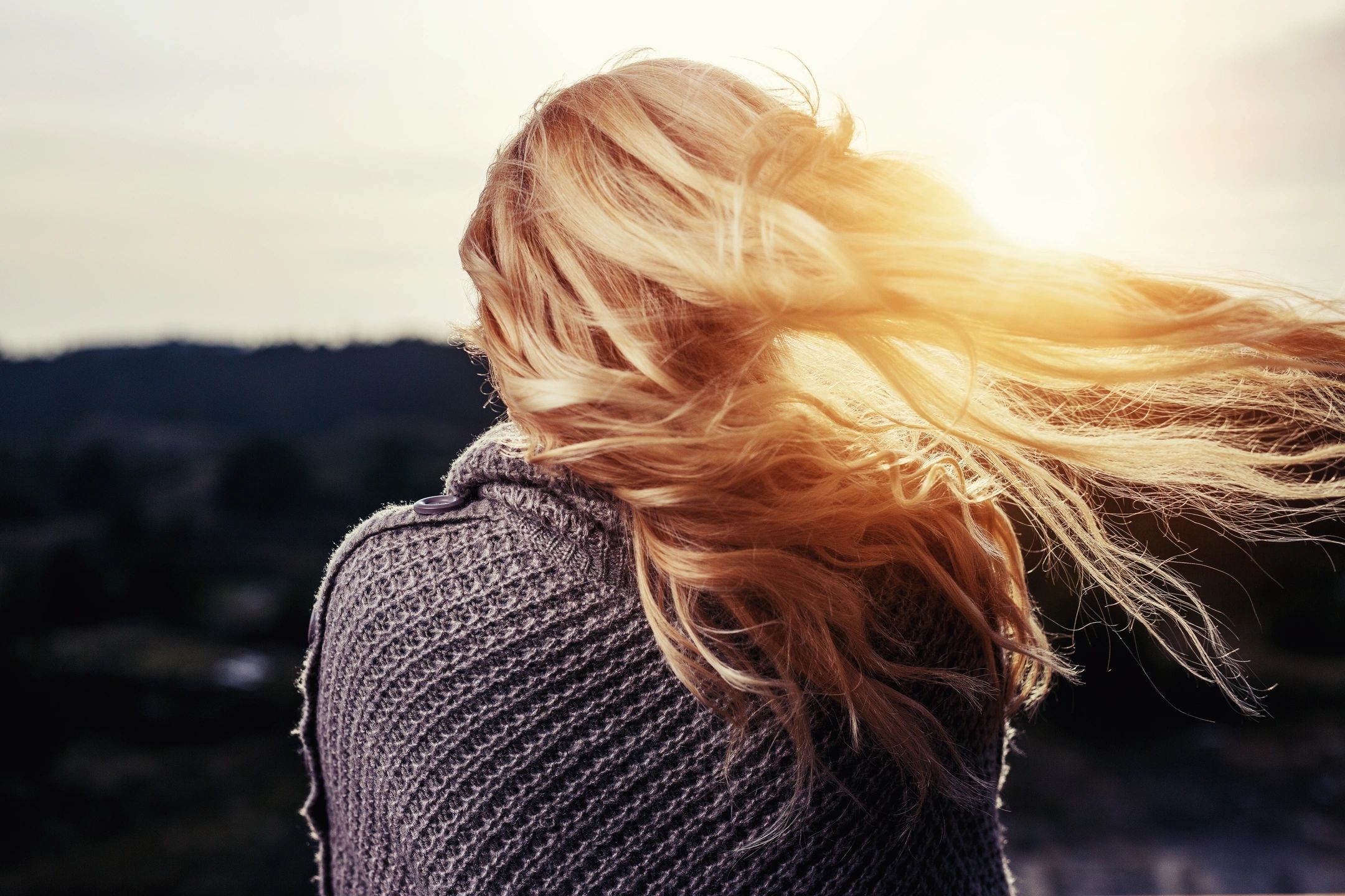 A woman standing with her back to the camera, gazing out over a vast, open field.