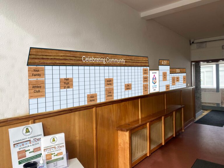 A hallway with a community recognition board titled "Celebrating Community," featuring sponsored plaques and spaces for future sponsors. A wooden bench runs along the wall, and a fundraising display on the left encourages donations to "Sponsor a Block."