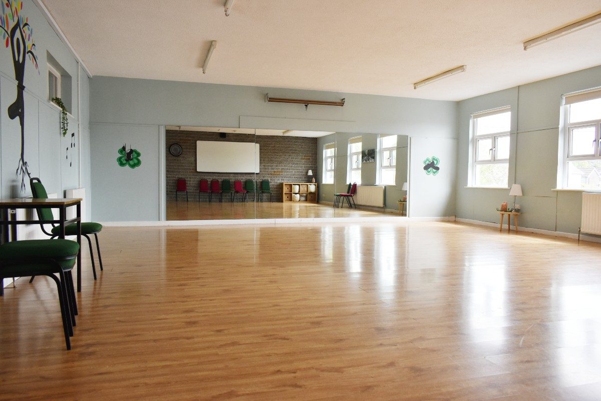 Physical activity room with mirrors, wooden floor, and green and red chairs.