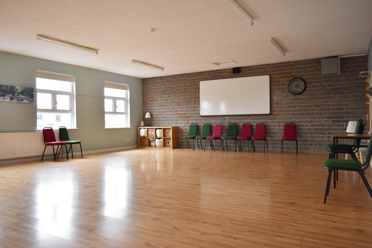 White board on wall in room with green and red chairs, wooden floor.