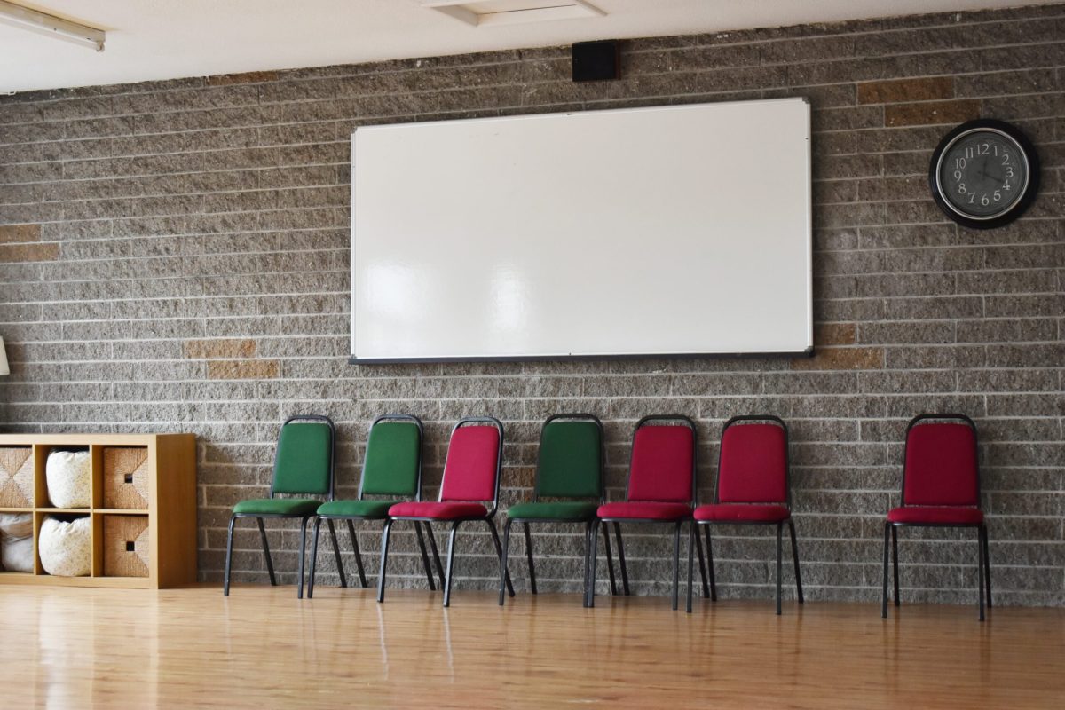 White board on wall in room with green and red chairs, wooden floor.