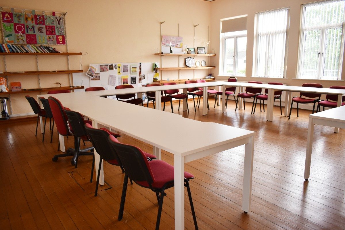 White tables in classroom with red chairs.