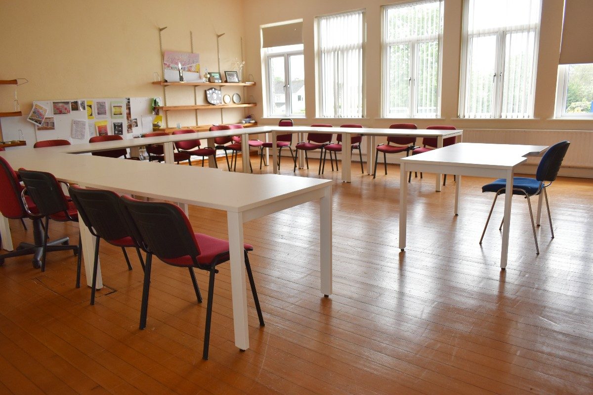 White tables in classroom with red chairs.