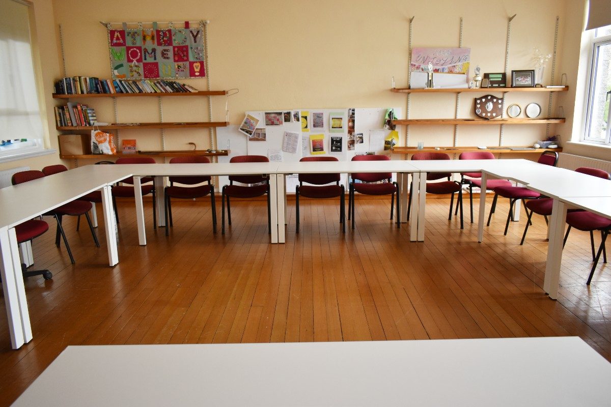 White tables in classroom with red chairs.