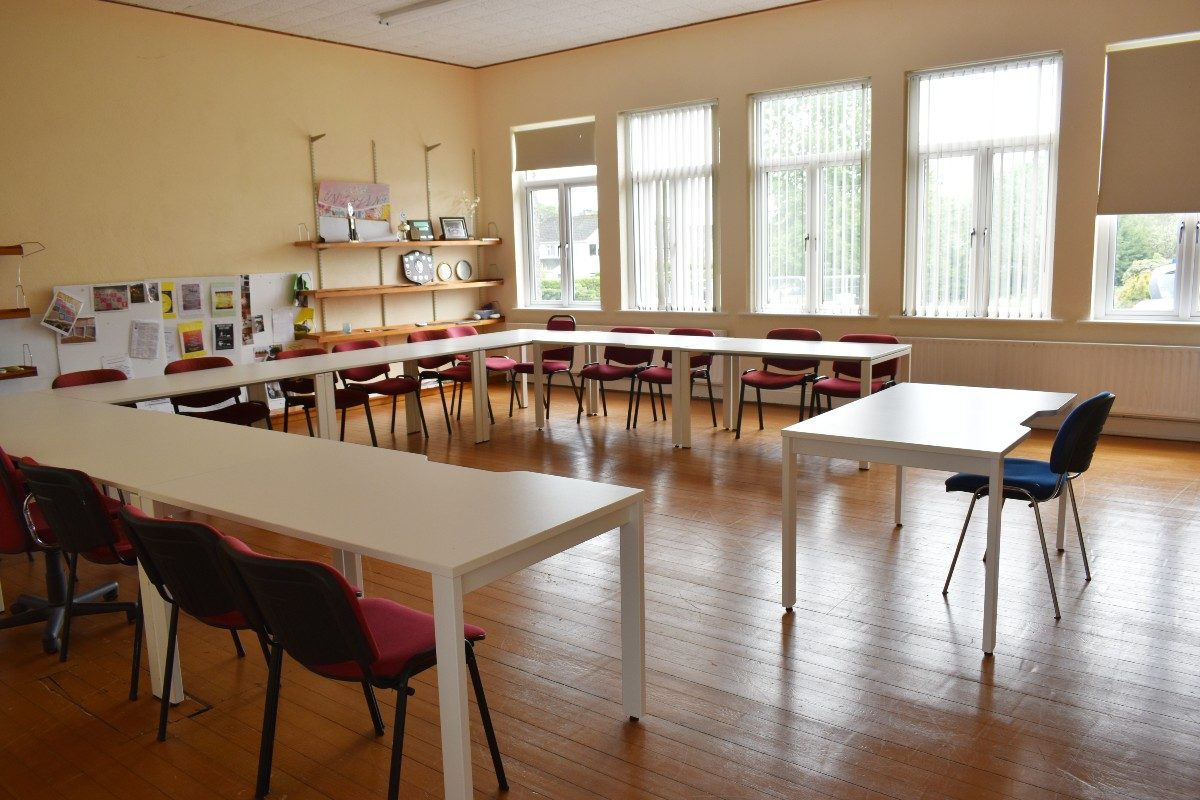 White tables in classroom with red chairs.