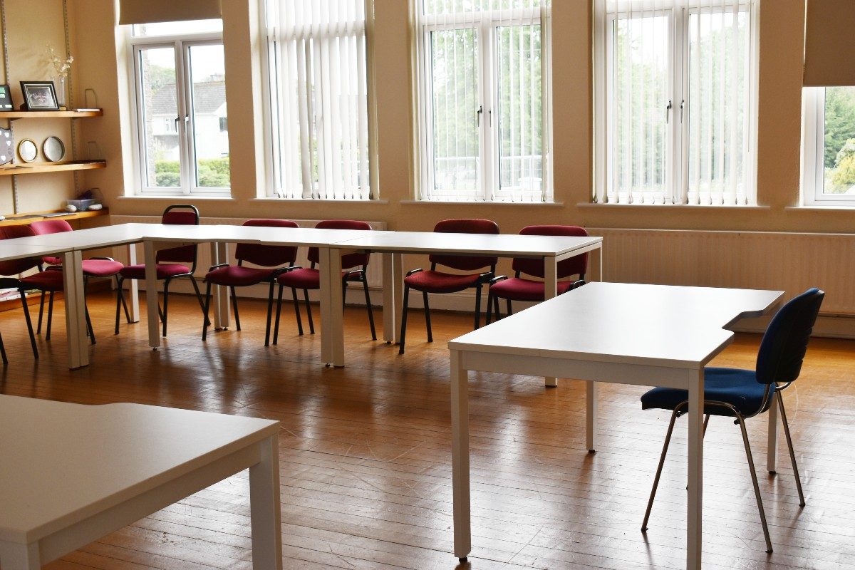 White tables in classroom with red chairs.