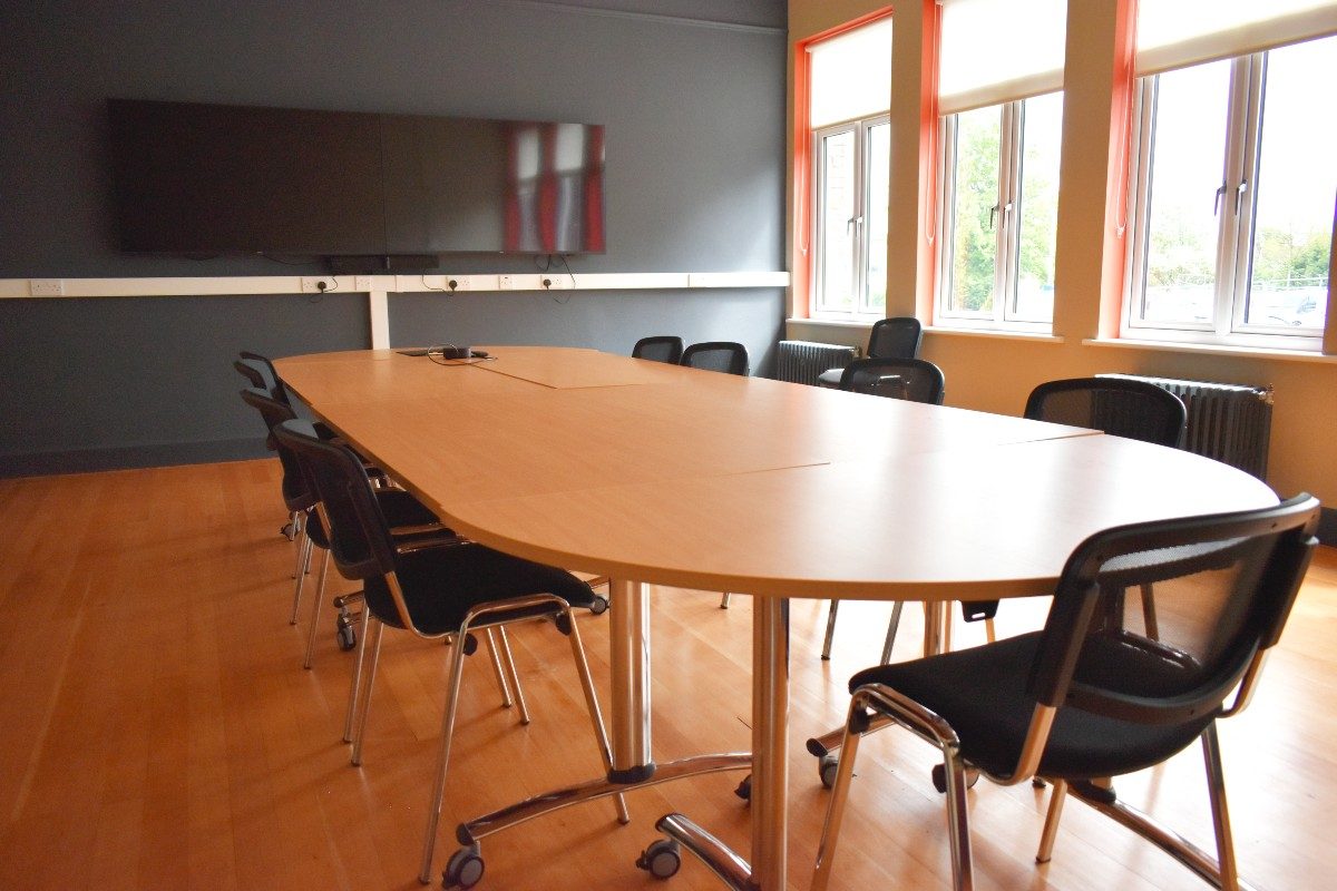 A conference table with chairs and a screen in a well-lit room, ready for a productive meeting.