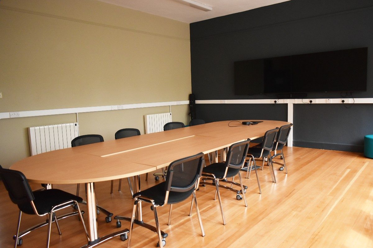 A conference table with chairs and a screen in a well-lit room, ready for a productive meeting.