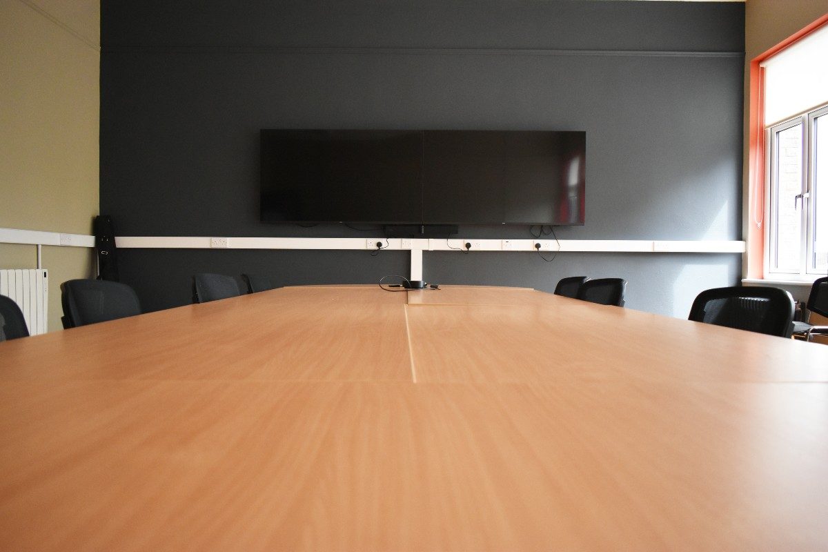 A conference table with chairs and a screen in a well-lit room, ready for a productive meeting.