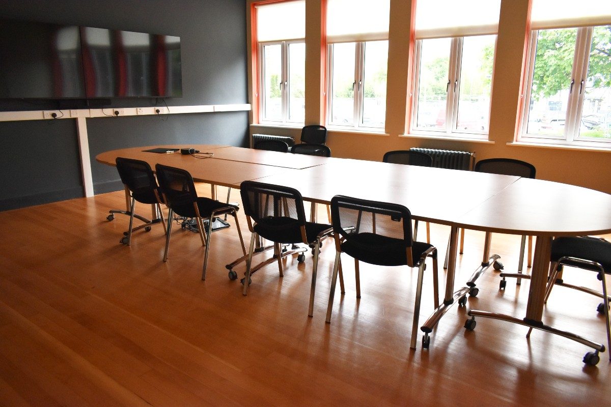 A conference table with chairs and a screen in a well-lit room, ready for a productive meeting.