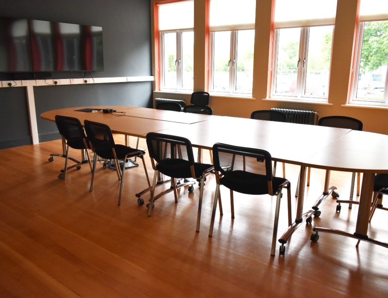 A conference table with chairs and a screen in a well-lit room, ready for a productive meeting.