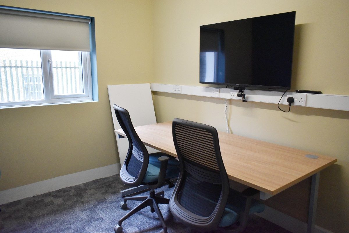 A desk and chair in a Zoom room with a flat screen TV.