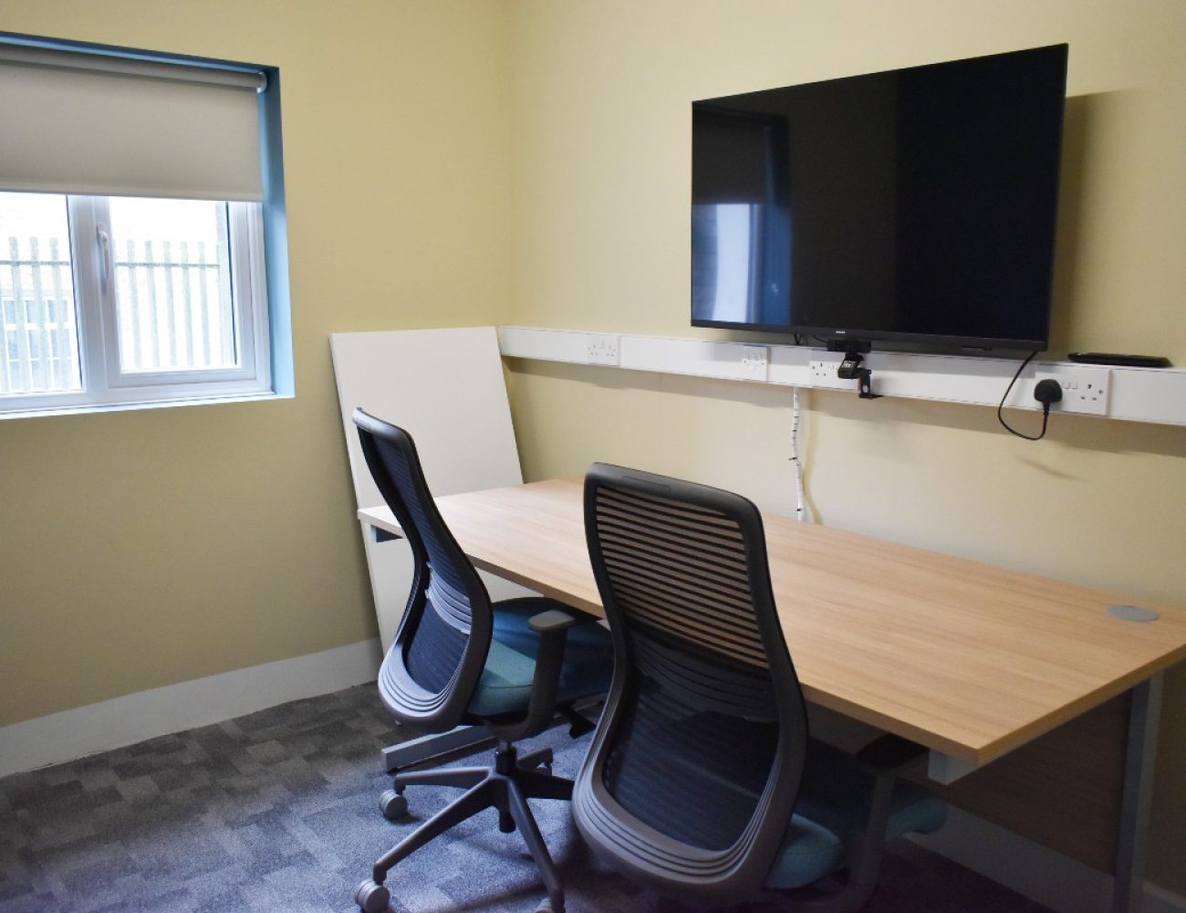 A desk and chair in a Zoom room with a flat screen TV.