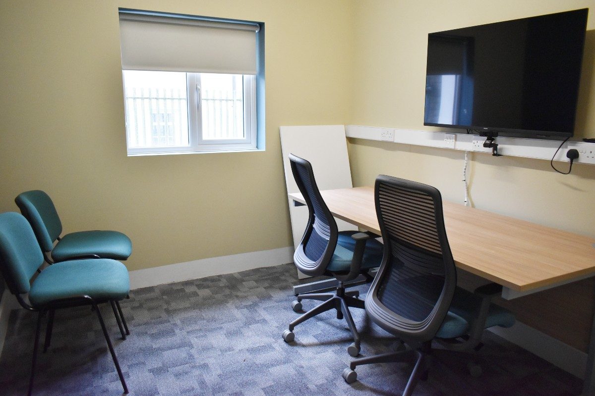 A desk and chair in a Zoom room with a flat screen TV.