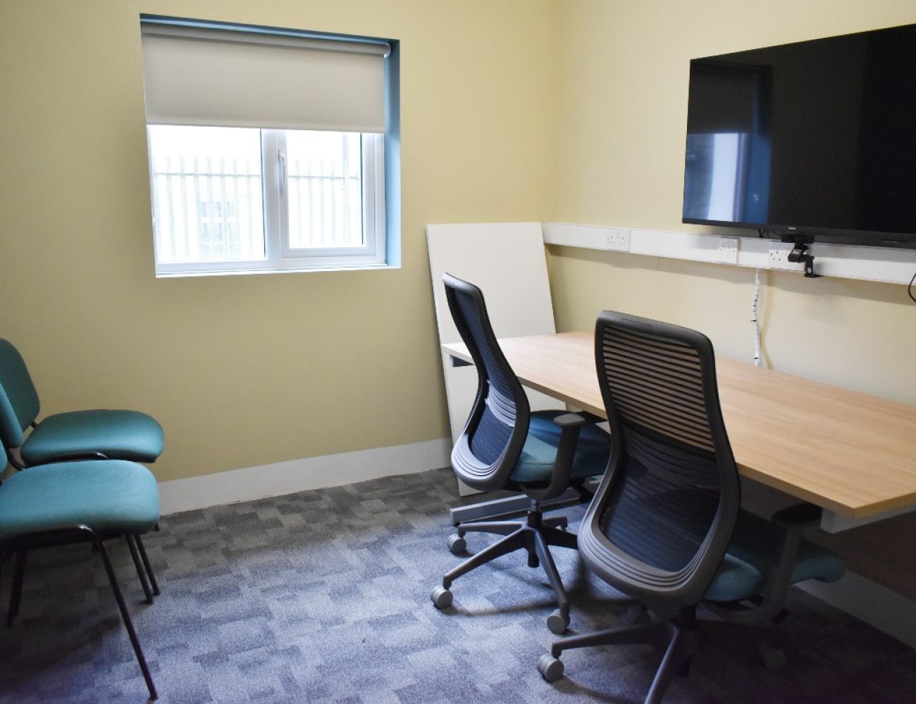 A desk and chair in a Zoom room with a flat screen TV.