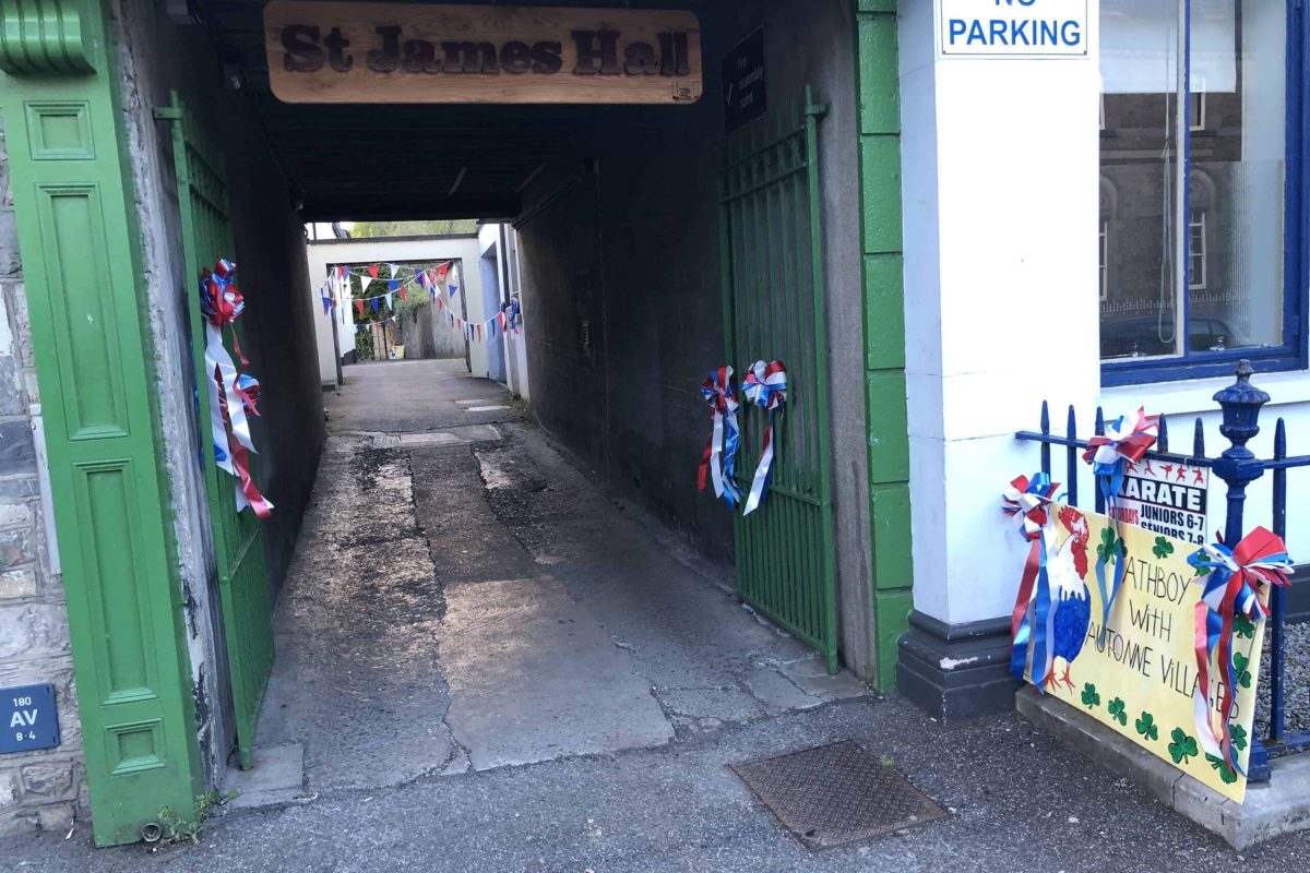 green gates with a wooden sign reading "St. James Hall" on it.