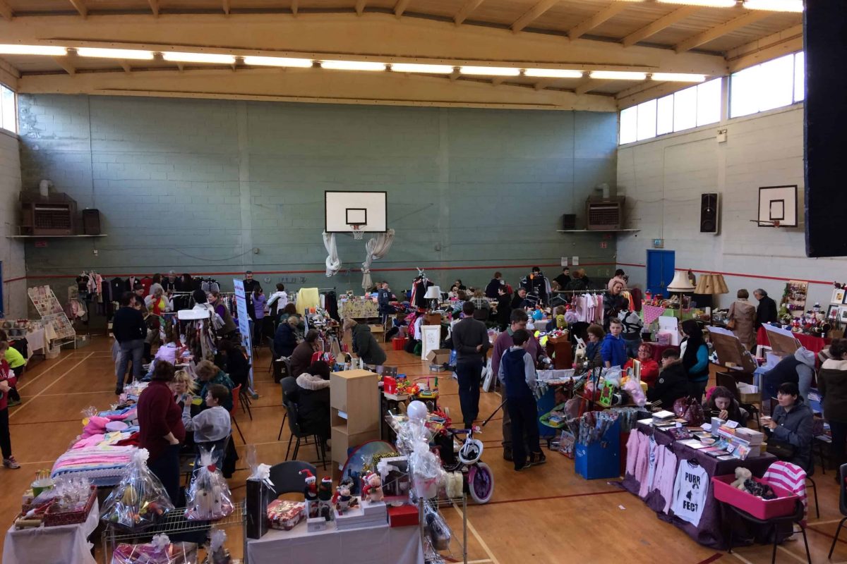 An indoor gymnasium filled with people and numerous tables for various activities.