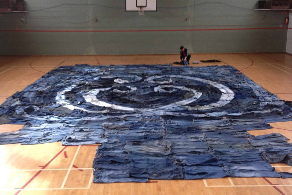 A person creating a large blue and white square art on the gymnasium floor.