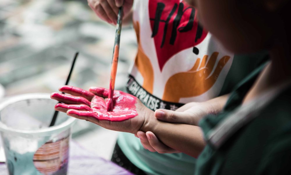 A kid painting another kids hand with pink paint.