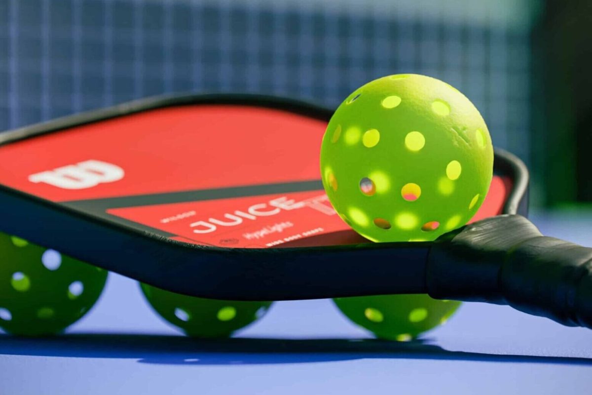 A pickle ball paddle with two balls resting on top.