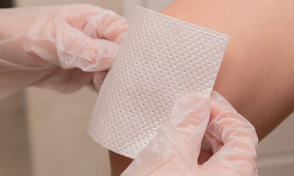 A nurse with latex gloves applying a plaster to a patient's arm.