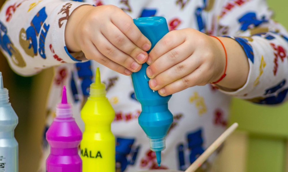 Kid squeezing a blue paint tube.