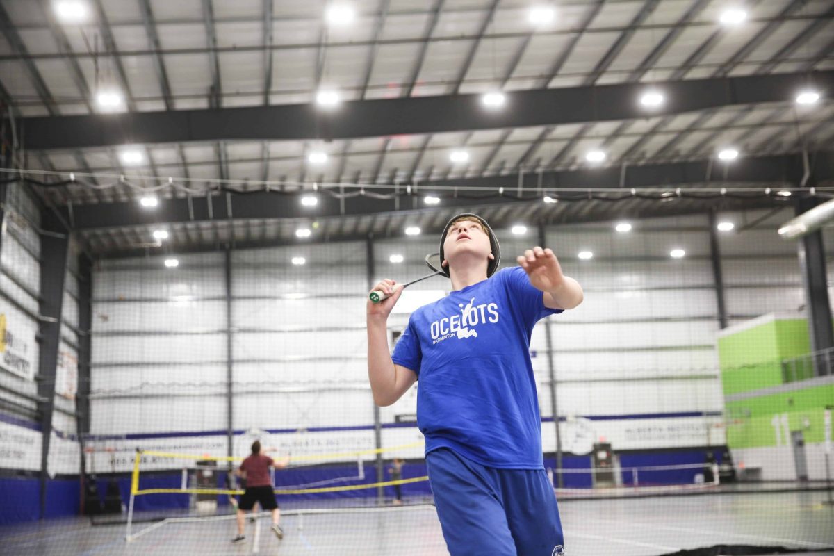 A young man in a blue shirt energetically playing badminton with a racket and shuttlecock.