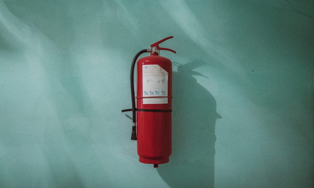 Red fire extinguisher mounted on green wall.