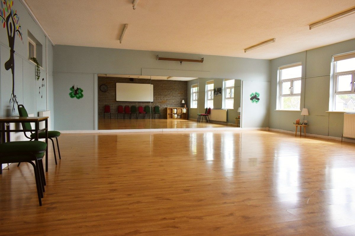 A spacious physical activity room at Athboy CCC with a mirrored wall and hardwood floors.