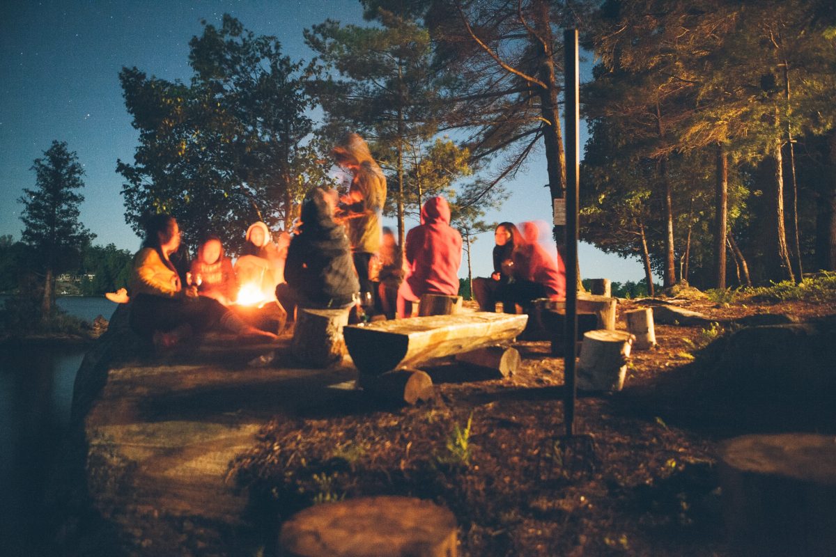 A group of people sitting around a campfire in the evening, enjoying their camping experience.